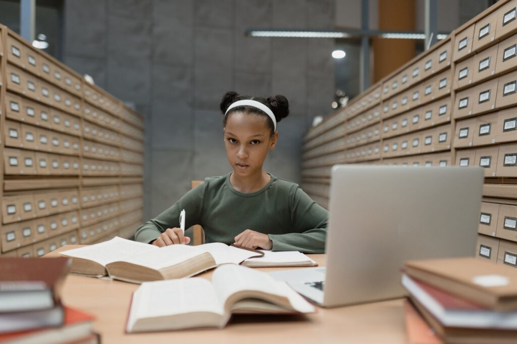 Student care lucrează la lucrarea de licență într-o bibliotecă, cu notițe și cărți pe birou