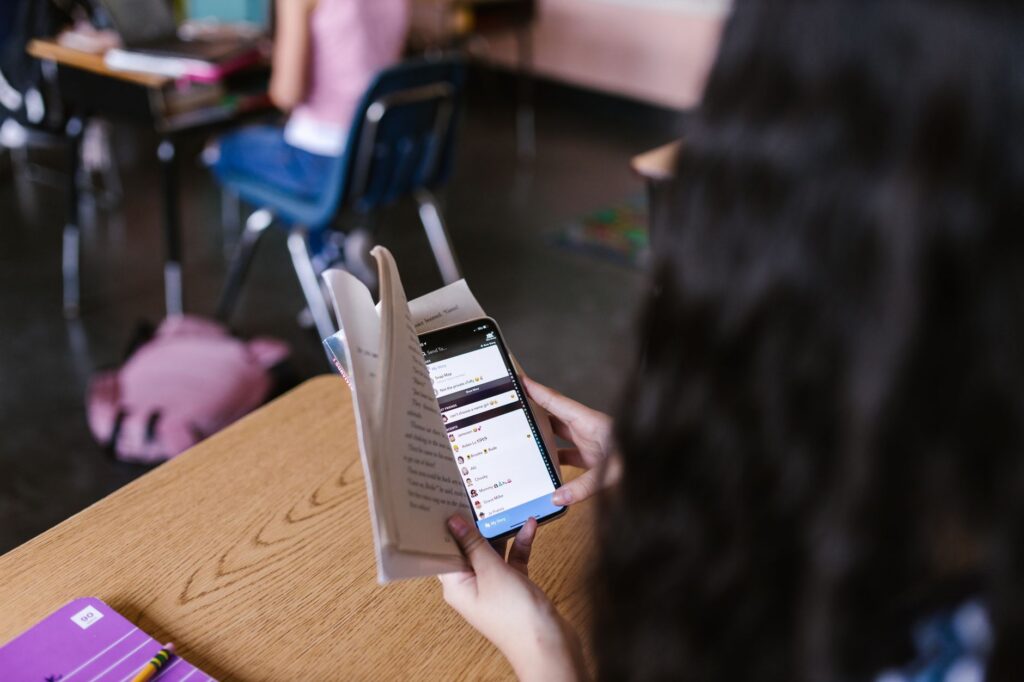 Student care citește atent o știre pe telefon, așezat pe o bancă în campusul universitar